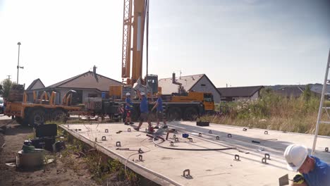 Construction-workers-installing-metal-beam-on-concrete-pad-from-crane