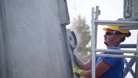 Bauarbeiter-Mit-Sonnenbrille-Schleift-Betonwand-Auf-Trittleiter