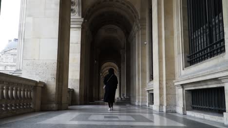 View-Behind-Female-Tourist-Walking-In-The-Arched-Hallway-Of-Louvre-Museum-In-Paris,-France