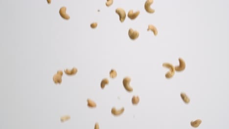 Whole-roasted-and-salted-cashew-nuts-raining-down-and-bouncing-back-into-frame-on-white-backdrop-in-slow-motion