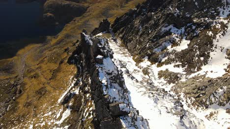 Aerial-tilt-down-shot-of-snow-on-rocky-peaks-on-mountain-lighting-by-sun---Molladalen-,Norway