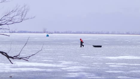 Fisher-men-waking-on-frozen-lake,-pulling-ice-sledge,-ice-fishing,-winter-cold-outdoor,-fishing-tent-on-frozen-lake,-mid-shot-Canada-wide-view-of-landscape