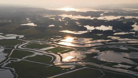 Sunrise-sunlit-flooded-agricultural-farmland-across-Sylhet,-Bangladesh,-Aerial-view-above-glowing-wetland