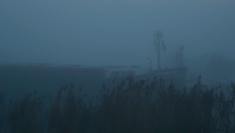 Bulk-carrier-ship-sailing-in-the-mysterious-morning-fog,-across-the-ferry-bay-of-Genemuiden,-Netherlands