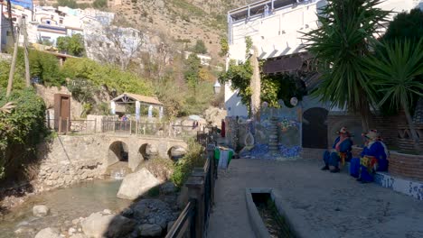 Chefchaouen-rural-landscape,-river-flowing-bellow-a-Stone-brigde,-People-resting-in-the-shade,-Pan-shot