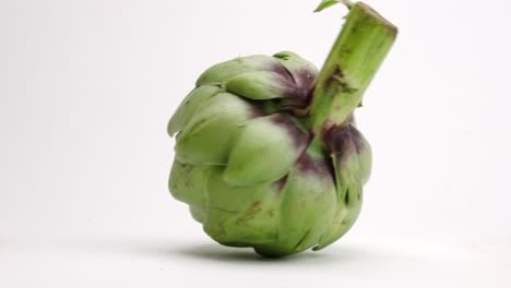 Fresh-cut-green-whole-artichoke-spinning-on-white-table-top-in-slow-motion
