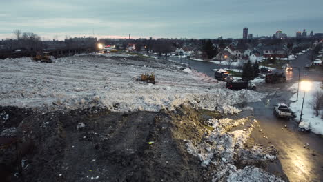 Aerial-Evening-Shot-Of-Trucks-Dumping-Excess-Snow-At-Storage-Site-In-Buffalo,-New-York