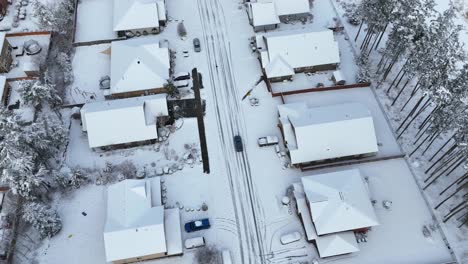 Overhead-drone-shot-of-an-SUV-driving-through-a-neighborhood-covered-in-snow