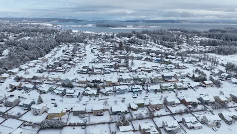 Drone-shot-of-an-American-neighborhood-covered-in-snow-with-the-ocean-on-the-horizon
