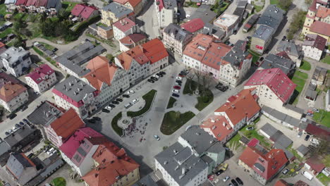 Top-down-view-of-market-square-in-old-European-town-surrounded-by-tenement-houses,-car-traffic-allowed,-people-gathered-at-the-fountain