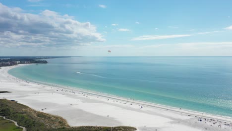 Aerial-view-of-Siesta-Key-beach-with-white-sand-and-turquoise-water,-paraglider-flying-above-the-beach