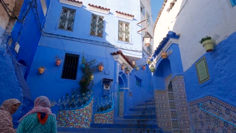 Damas-Marroquíes-En-La-Típica-Escalera-De-Callejón-De-Color-Azul-En-El-Casco-Antiguo-De-Chefchaouen,-Marruecos,-Tiro-Inclinado-Hacia-Abajo