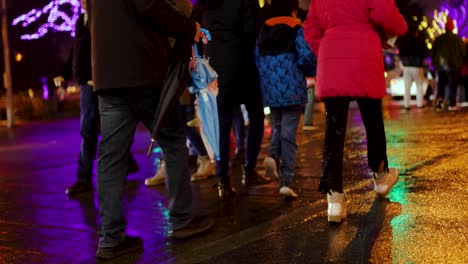 People-crossing-wet-street-at-night-with-bright-lights-and-charisms-and-new-year-decorations,-footpath,-Niagara-Falls-Canada
