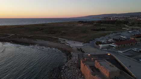 Aerial-scenic-view-over-Kato-Paphos-Castle-into-sunset-skyline,-Cyprus