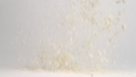 White-flour-falling-onto-white-studio-backdrop-surface-and-piling-up-in-4k-slow-motion