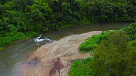 The-drone-glides-above-the-meandering-tropical-river,-tracing-its-winding-path-through-lush-vegetation