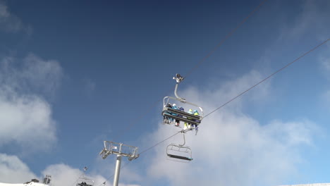 Fully-occupied-ski-chair-lift-unit-crossing-frame-with-blue-sky-and-fluffy-clouds