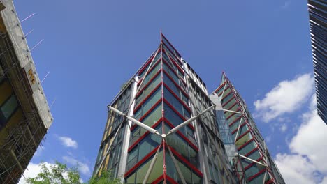 Modernes-Gebäude-Mit-Dunkelgrün-Getönten-Fenstern,-Roten-Linien,-Sehr-Herausragende-Ikonische-Architektur-Mitten-In-London,-Und-Das-Gebäude-An-Der-Seite-Ist-In-Arbeit.-Baum-Unten,-Wunderschöner-Himmel