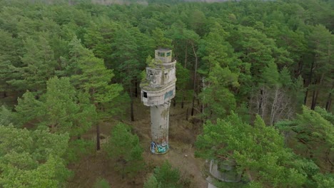 Establishing-aerial-view-of-old-Soviet-military-concrete-observation-watchtower,-pine-tree-forest,-Liepaja-,-military-heritage,-Nordic-woodland,-wide-drone-shot-moving-forward,-tilt-down