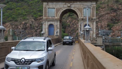 Tilt-down-from-stone-arch-over-Hartbeespoort-Dam-to-cars-driving-over