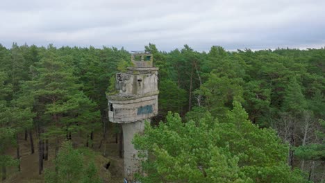 Establishing-aerial-view-of-old-Soviet-military-concrete-observation-watchtower,-pine-tree-forest,-Liepaja-,-military-heritage,-Nordic-woodland,-wide-descending-drone-shot