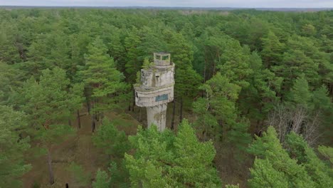 Establishing-aerial-birdseye-view-of-old-Soviet-military-concrete-observation-watchtower,-pine-tree-forest,-Liepaja-,-military-heritage,-Nordic-woodland,-wide-orbiting-drone-shot