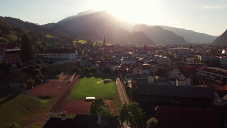 Sunset-flight-over-Lucerns-town-area,-showing-roofs-and-towering-mountains