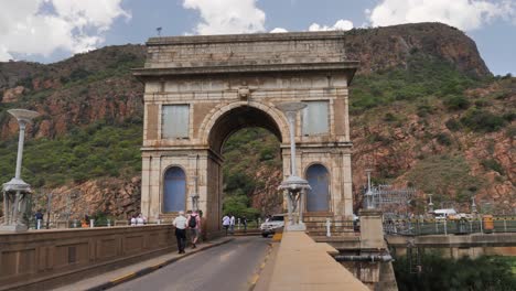 Los-Visitantes-Caminan-Y-Conducen-A-Través-Del-Arco-De-Piedra-Sobre-La-Presa-Hartbeespoort