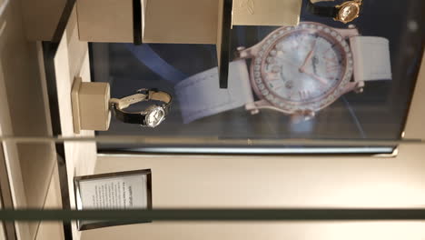 Luxury-watch-displayed-on-shop,-vertical-close-up,-behind-glass-with-poster