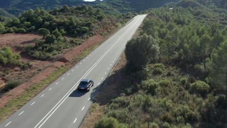 Aerial-view-following-classic-BMW-sportscar-driving-through-long-straight-woodland-road