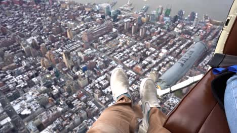 Feet-hanging-out-from-a-Helicopter-above-Manhattan,-New-York---POV-shot