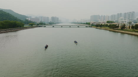 Drone-approaching-a-bridge-over-a-river-with-boats-rowing-over-the-water