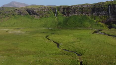 Meadow-and-mountain-landscape-with-small-waterfall-stream-in-Iceland,-aerial-drone-view