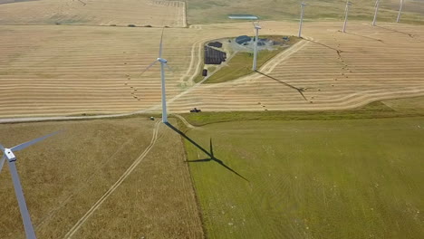 Hay-bales-line-up-in-field-below-spinning-wind-turbines-in-wind-farm