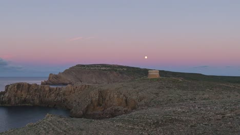 Rosafarbener-Sonnenuntergangshimmel-über-Fornells-Auf-Menorca,-Spanien,-Mit-Filmischem-Flug-Um-Den-Alten-Verteidigungsturm