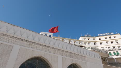 Looking-Up-At-Moroccan-Flag-On-Pole-Above-Murailles-Historiques-With-View-Of-Hotel-Continental-In-Background-In-Tangier