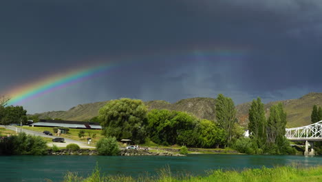 Bridge-near-town-Alexandra-in-New-Zealand-with-massive-dark-storm-clouds-and-rainbow-above,-pan-left-view