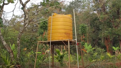 Bright-yellow-water-tank-on-tower-with-green-forest-background