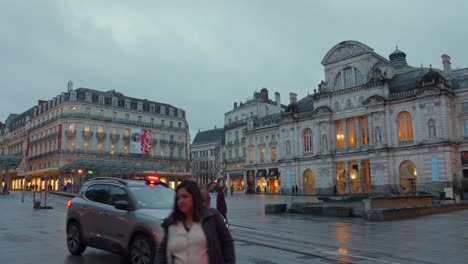 Pedestrians-And-Car-In-Front-Of-Grand-Theater-At-Night-In-Maine-et-Loire,-Place-du-Ralliement,-Angers,-France