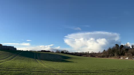 Green-sunlit-shadowy-farm-field,-tractor-traces,-puffy-cloud-mushroom-shaped,-UK