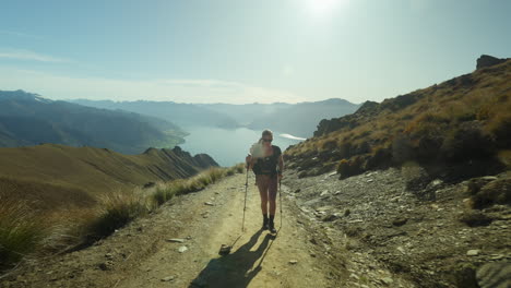 Fit-active-woman-walking-up-steep-mountain-path-towards-Isthmus-Peak,-bright-sunshine