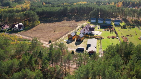 Aerial-Flying-Over-Woodland-Trees-Showing-Clearing-And-Multiple-Buildings-With-Barn