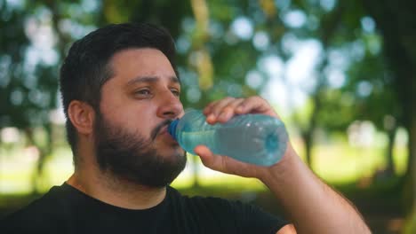 Close-up-young-man-drinks-water-from-bottle-after-jogging-in-park-young-healthy-person-active-training-lifestyle