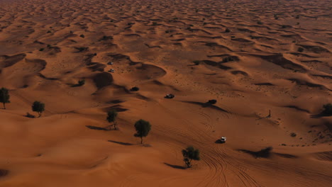 Aerial-View-Of-Offroad-Vehicles-Driving-Across-Vast-Desert,-Navigating-The-Rough-Terrain-On-A-Sunny-Day