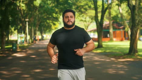Front-view-following-man-jogging-at-the-park-on-a-sunny-summer-day-slow-motion