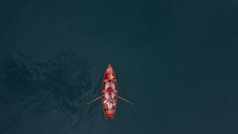 Top-down-aerial-view-of-a-people-paddling-in-a-red-paddling-boat-on-the-deep-turquoise-alpine-lake-Thunersee-in-Switzerland