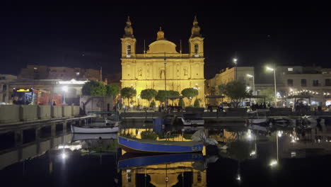 Limestone-Church-St-Joseph's-Church-in-Msida-seen-from-the-port-where-people-keep-their-boats,-at-night