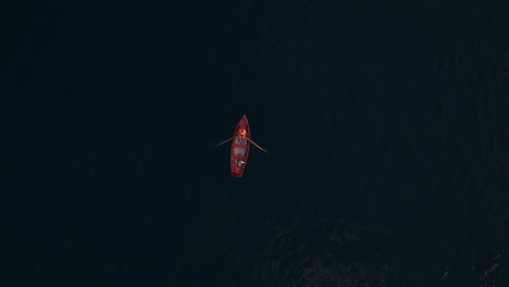 Top-down-view-of-a-red-paddling-boat-in-a-deep-dark-blue-lake
