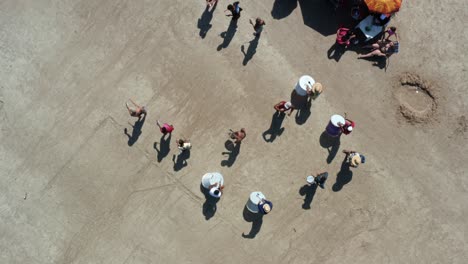 Bird's-eye-rotating-aerial-drone-shot-of-a-marching-band-and-teens-dressed-as-furry-bears-performing-and-asking-for-money-for-Carnaval-on-the-tropical-Bessa-beach-in-Joao-Pessoa,-Paraiba,-Brazil