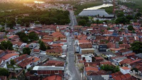 dolly-in-aerial-drone-shot-of-a-small-road-with-traffic-in-the-old-historic-downtown-of-the-tropical-coastal-capital-city-of-Joao-Pessoa,-Paraiba,-Brazil-with-houses,-cars,-and-factories-during-sunset